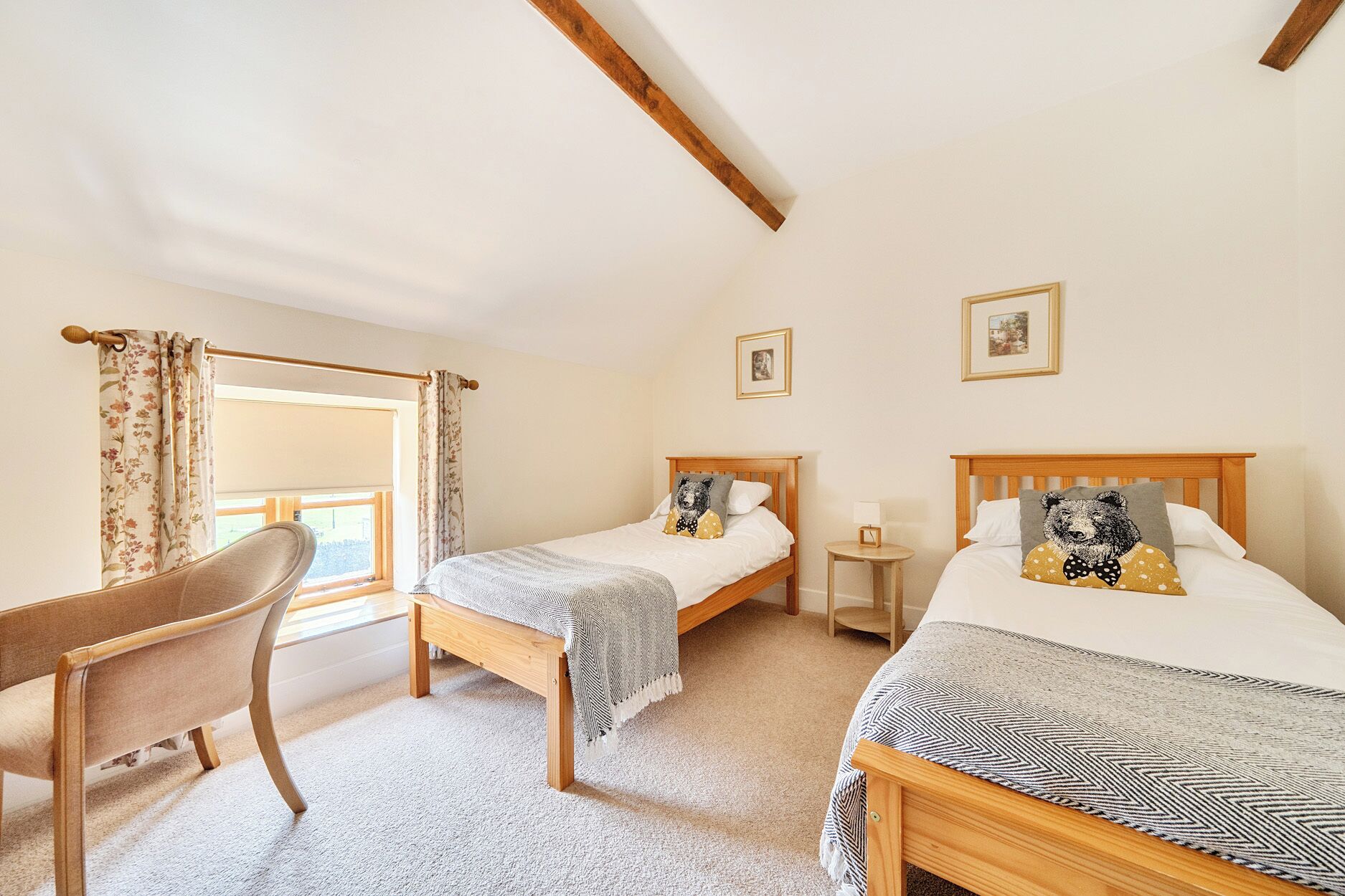 A bedroom with two wooden beds, a wooden chair, a small bedside table, and a window with curtains.