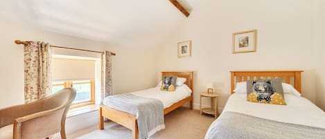 A bedroom with two wooden beds, a wooden chair, a small bedside table, and a window with curtains.