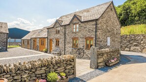 A stone building with multiple doors and windows, a bicycle, and a stone wall with flowers. - The Dairy (Corwen)