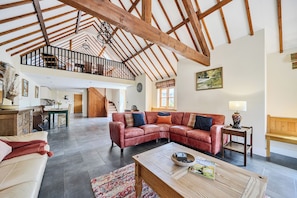 Un loft espacioso con vigas de madera a la vista, un amplio sofá de cuero en forma de L, una mesa de centro y un comedor.