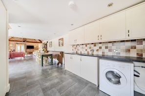 A kitchen with a washing machine, a dining area with a bench, and a living room with a sofa. - The Dairy (Corwen)
