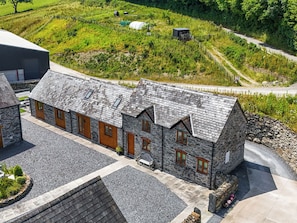 A stone building with a sloped roof, multiple windows, and a gravel driveway. - The Dairy (Corwen)