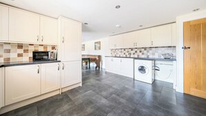 A modern kitchen with white cabinets, a microwave, and a washing machine. - The Dairy (Corwen)