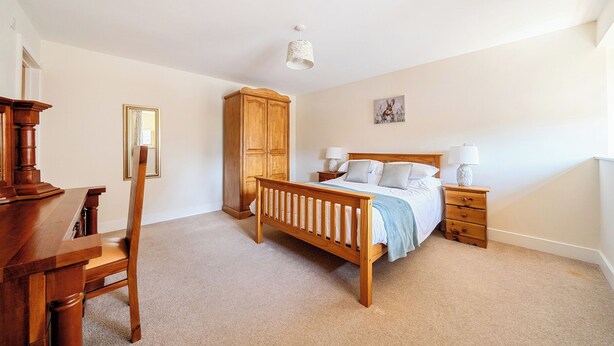 A bedroom with a wooden bed, a desk, a chair, a wardrobe, and a nightstand with lamps. - The Dairy (Corwen)