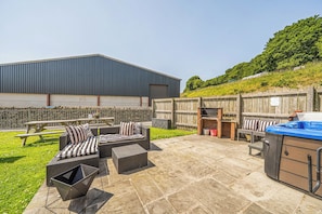 An outdoor patio area with a barbecue grill, wicker furniture, and a large building in the background. - The Dairy (Corwen)