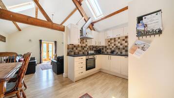 A spacious kitchen with wooden beams, a dining area with a table and chairs, and a view through a glass door.