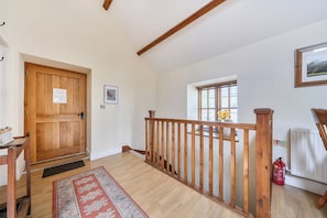 A wooden staircase with a handrail leading to a second floor, a wooden door with a notice, a framed picture on the wall, and a window with blinds. - The Granary (Corwen)