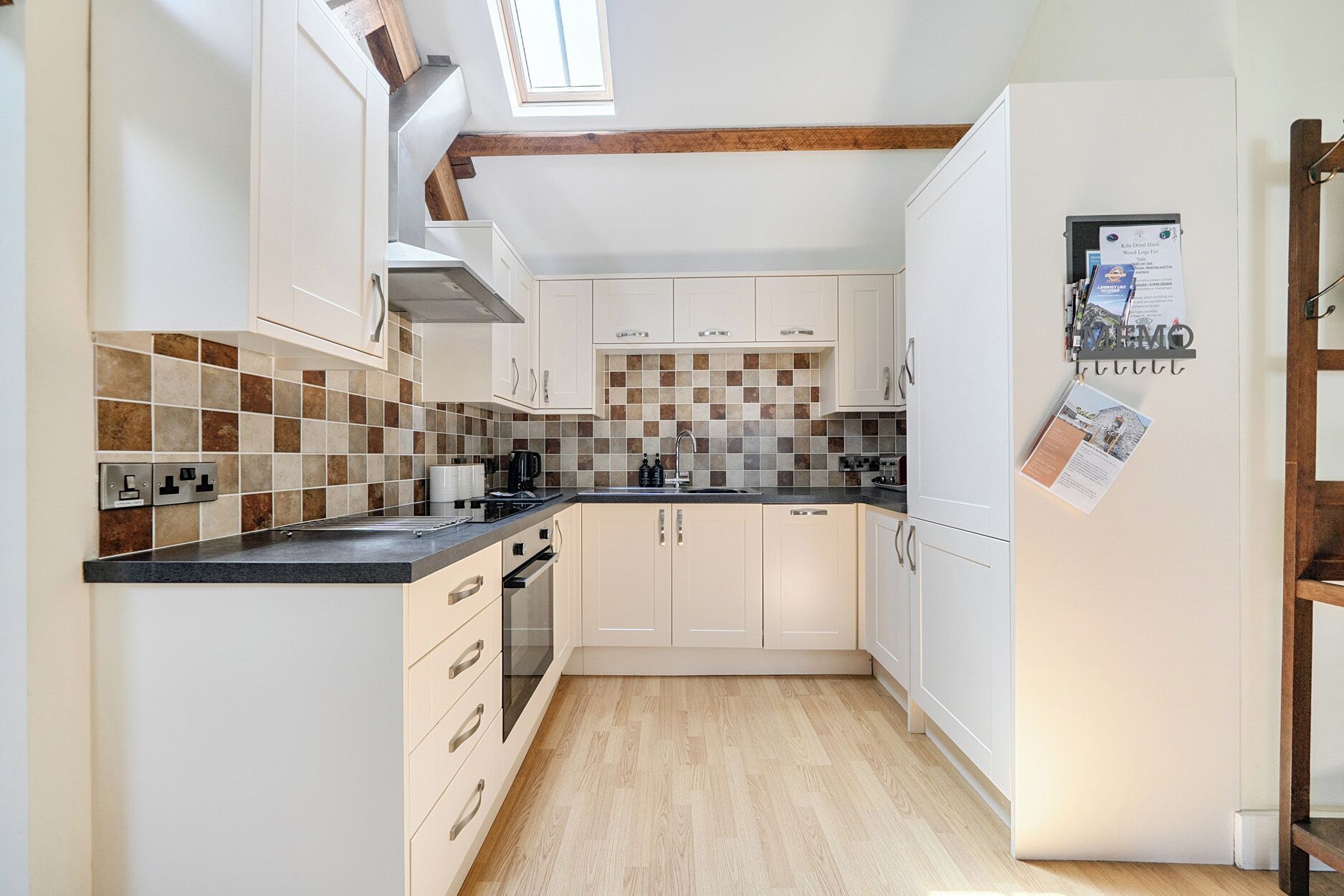 Una cocina con armarios blancos, encimera negra y salpicadero de azulejos.