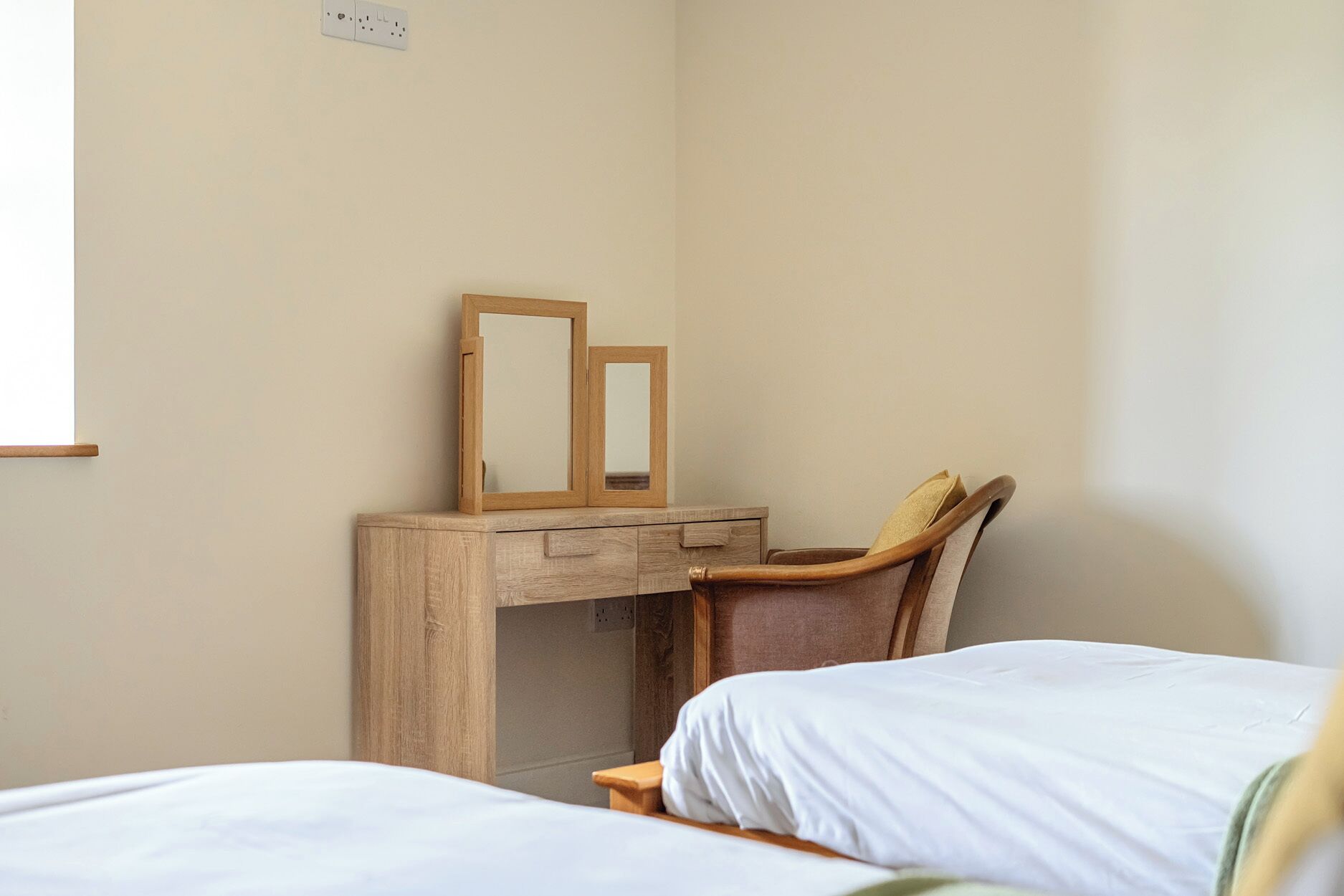 A bedroom with a wooden desk, two mirrors, a chair, and two beds.
