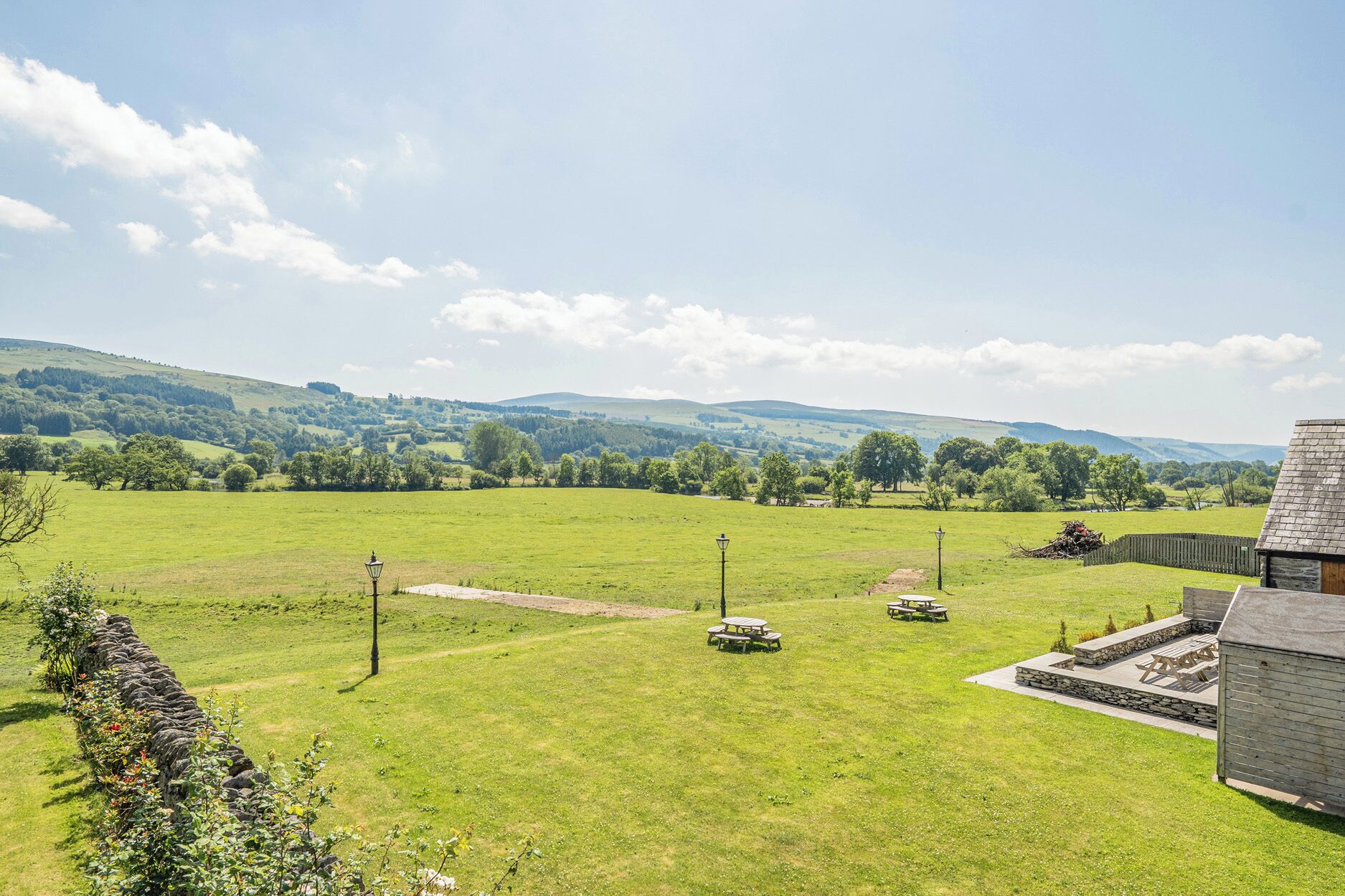 A grassy field with stone walls, picnic tables, and a stone building.