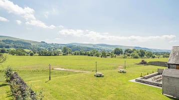 A grassy field with stone walls, picnic tables, and a stone building.