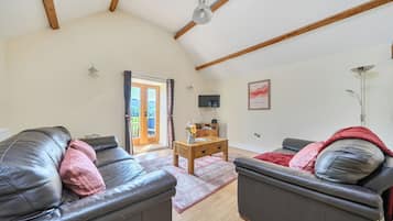 A spacious living room with a high ceiling, a sliding glass door leading to a balcony, a flat-screen TV mounted on the wall, and a wooden coffee table.