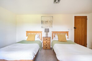 A room with two wooden beds, a nightstand with a lamp, a wooden door, and a framed picture on the wall. - The Granary (Corwen)