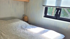 Un dormitorio con una cama, una ventana y una lámpara fijada a la pared.