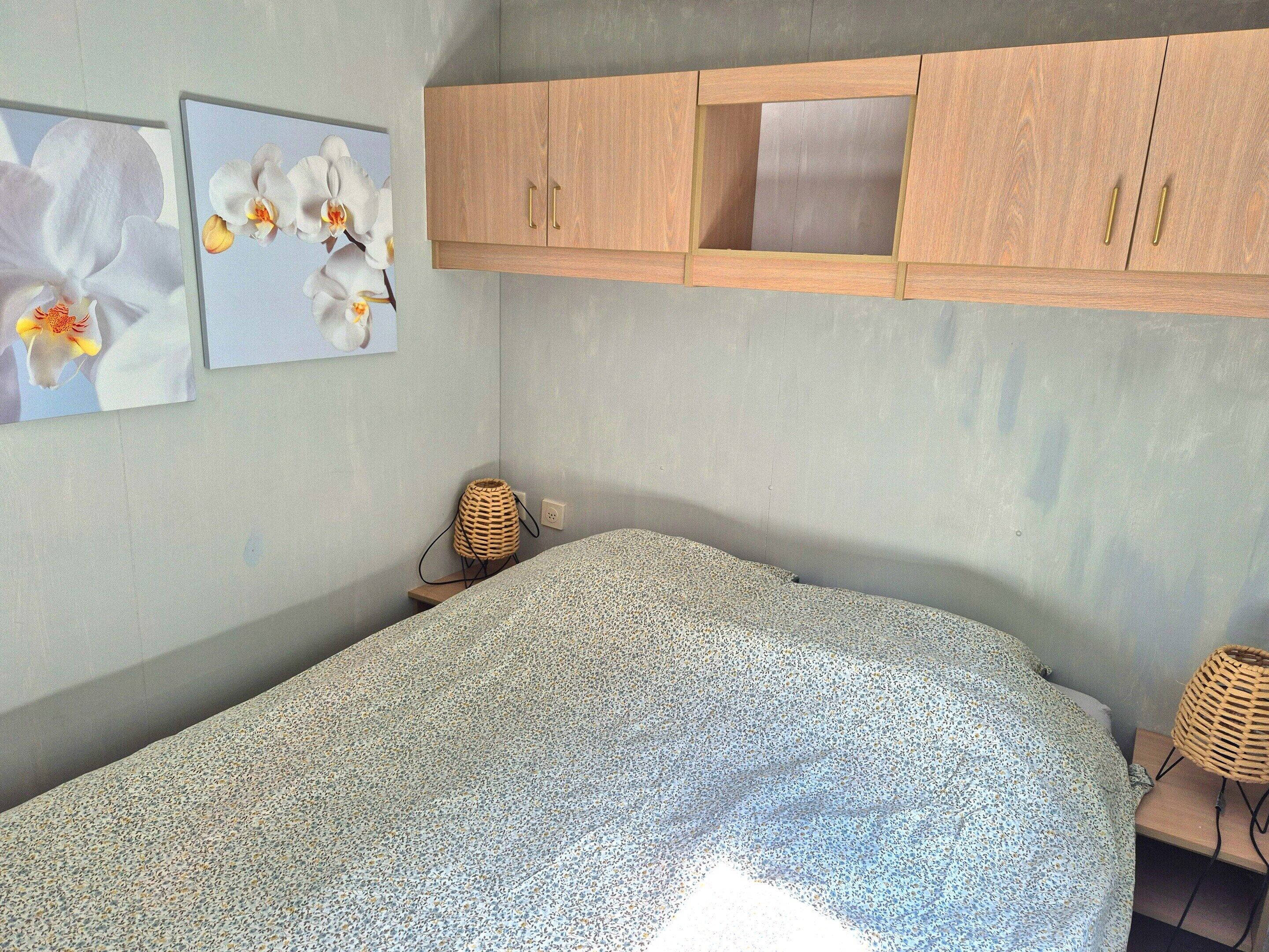 A bedroom with a bed, a wooden wardrobe, and two wall-mounted lamps.