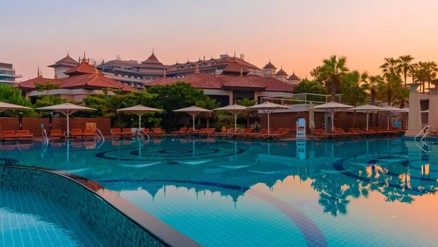 Ein Swimmingpool mit Liegestühlen und Sonnenschirmen, umgeben von Gebäuden mit traditioneller Architektur.