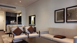 Ein modernes Wohnzimmer mit Sofa, Sesseln, einem Couchtisch und einer Küche im Hintergrund.