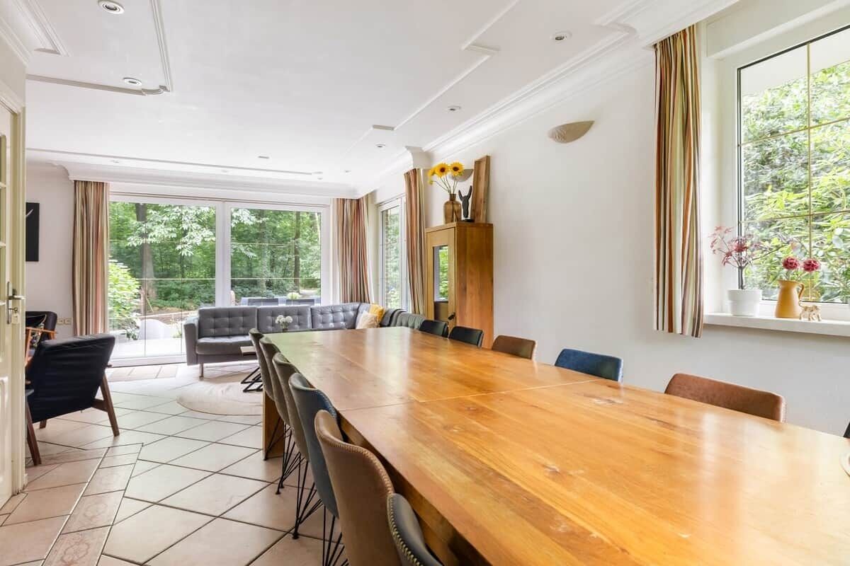 Een ruime kamer met een grote houten tafel, een bank en een raam met gordijnen.