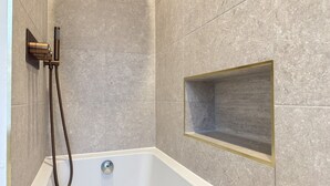 Ein Badezimmer mit einer Badewanne, einer Duschbrause und einem integrierten Ablagefach.