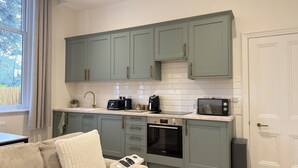 Eine Küche mit hellgrünen Schränken, einer weißen Fliesenspiegel, einem eingebauten Backofen, einer Mikrowelle und einer Kaffeemaschine.