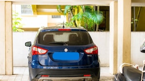 A blue car parked in a covered parking area with tiled flooring and a scooter nearby.