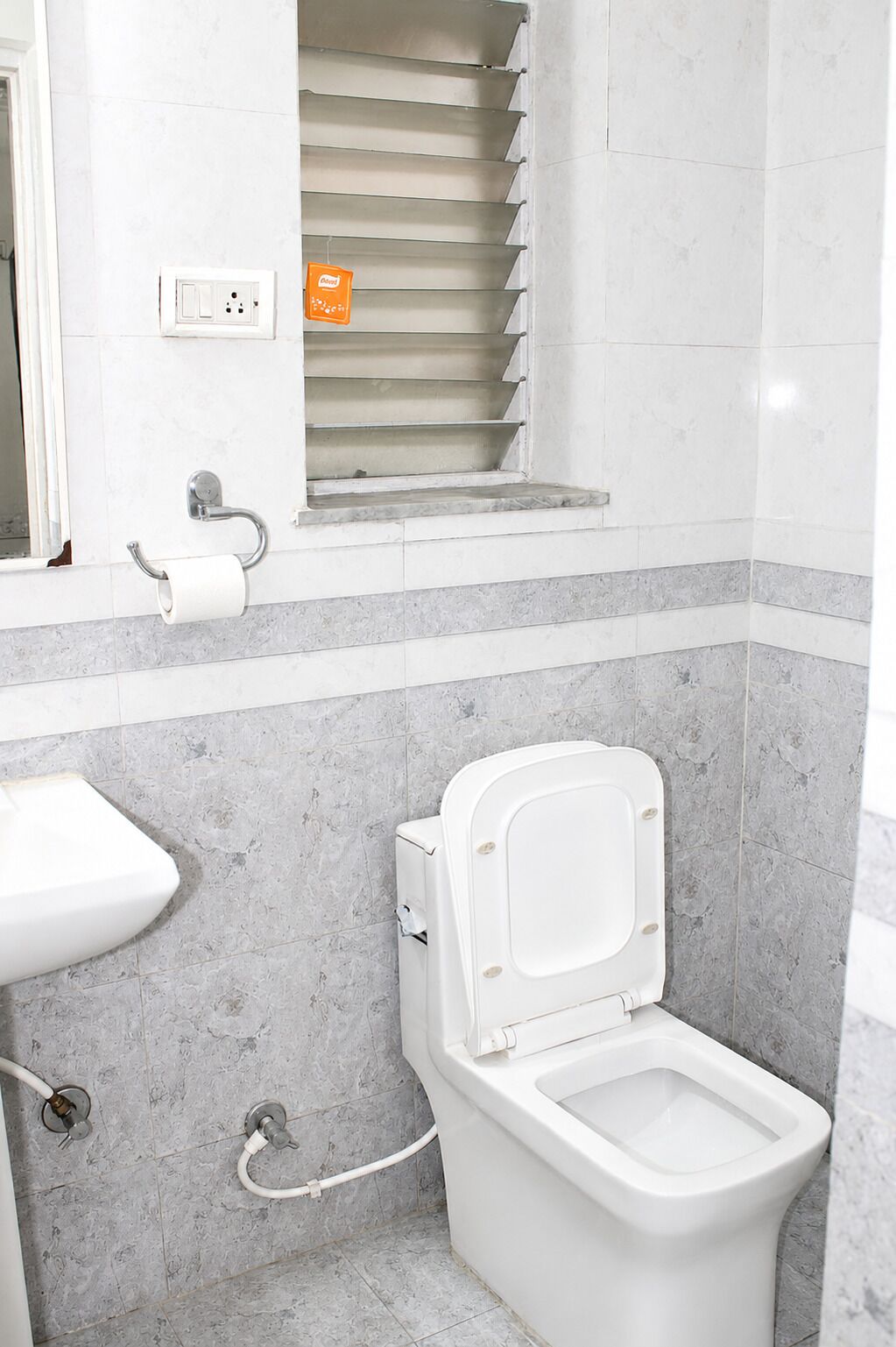 A bathroom with a toilet, a sink, and a window with a towel rack.