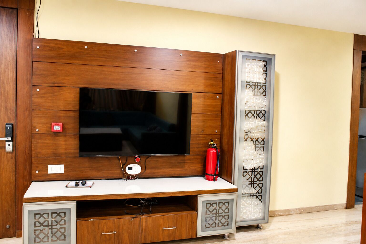 Un mueble de madera con un televisor de pantalla plana, un extintor y un panel decorativo.