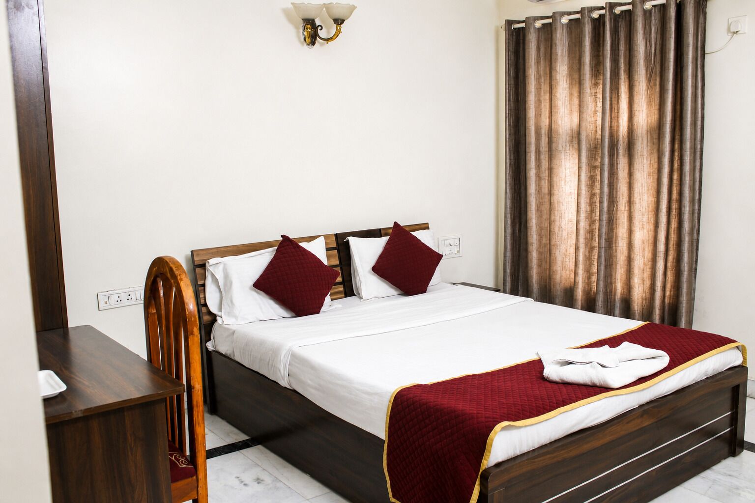 A neatly made bed with a white and red bedspread, a wooden headboard, and two red pillows.