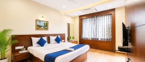 A modern hotel room with a wooden bed, a ceiling fan, a large window with curtains, a flat-screen TV, and a potted plant.