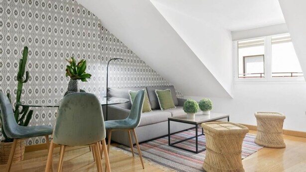 A modern loft with a sloped ceiling, a grey sofa, two armchairs, a coffee table, and a patterned wall. - Madrid Hideaway Near Museums (Madrid)