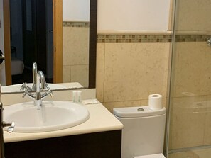 Ein Badezimmer mit Waschbecken, Spiegel, Toilette und Duschkabine aus Glas.