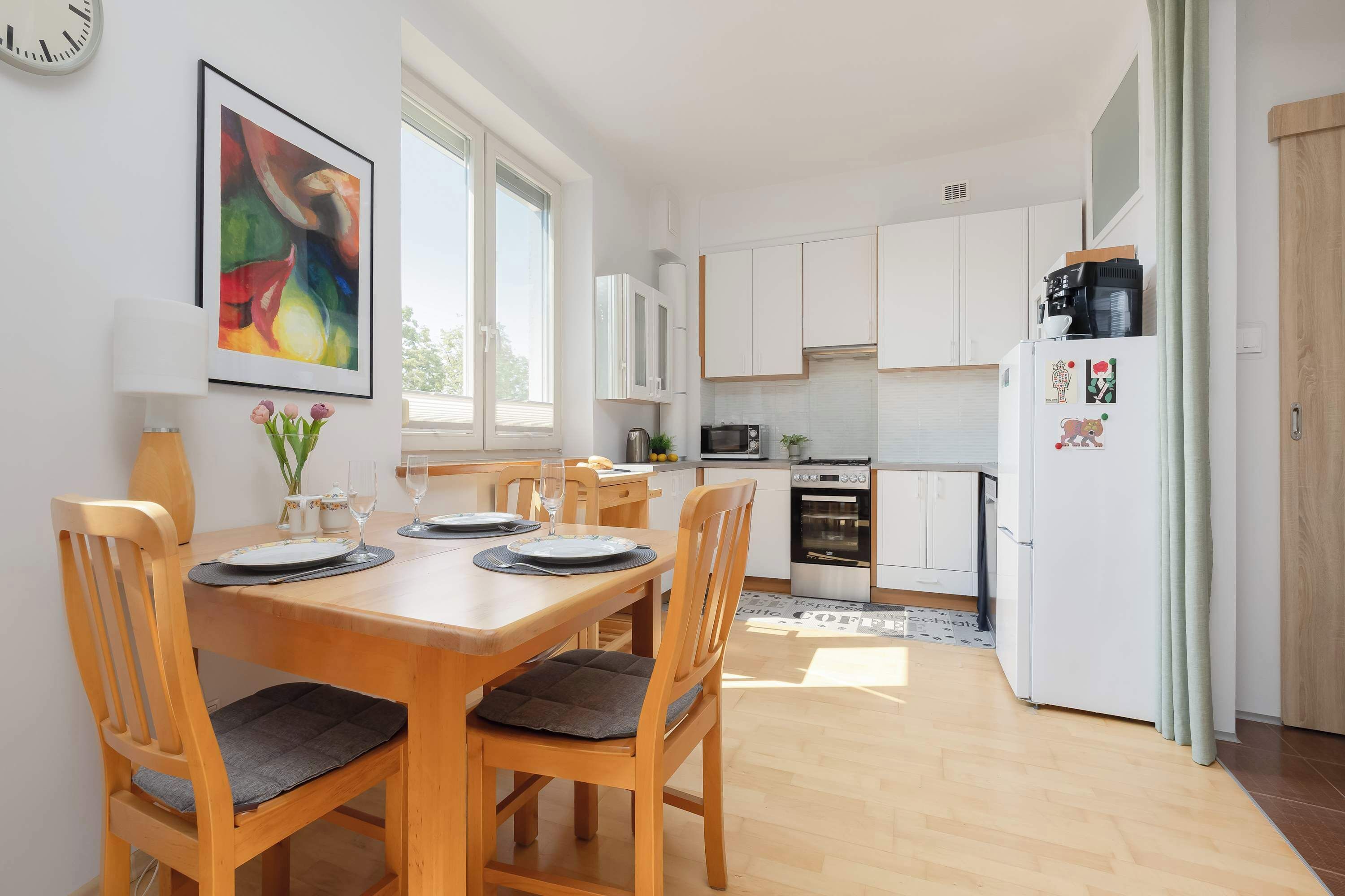 A modern kitchen with white cabinets, a dining table set for four, and a refrigerator with magnets.