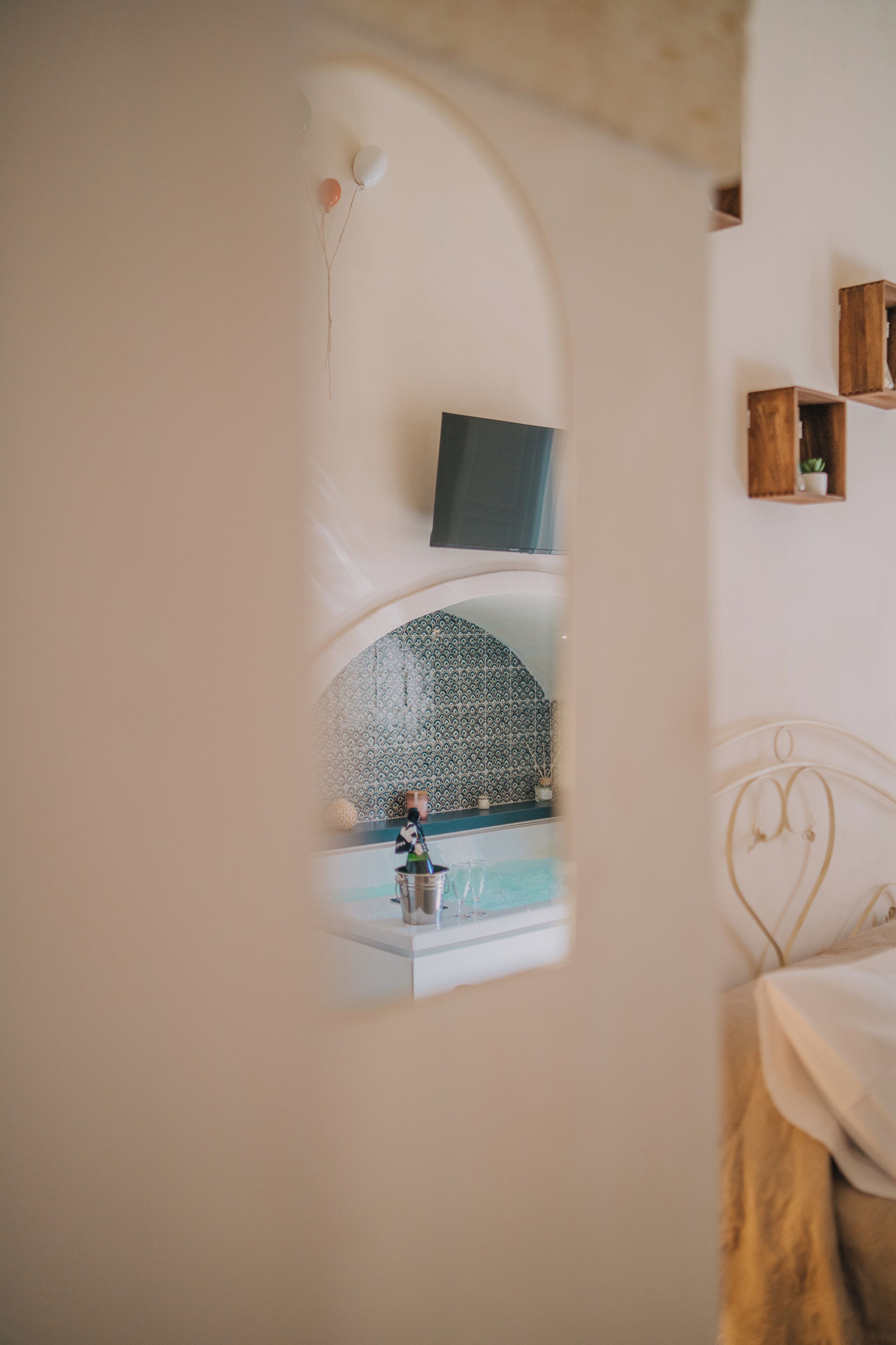 Una habitación con cama, una mesita con una botella, un televisor de pared y un papel tapiz decorado.
