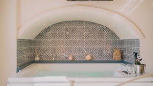 A bathroom with a bathtub, a tiled wall, and a shelf with various items.