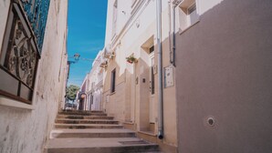 A narrow street with steps leading to a building with a white facade and a blue door.