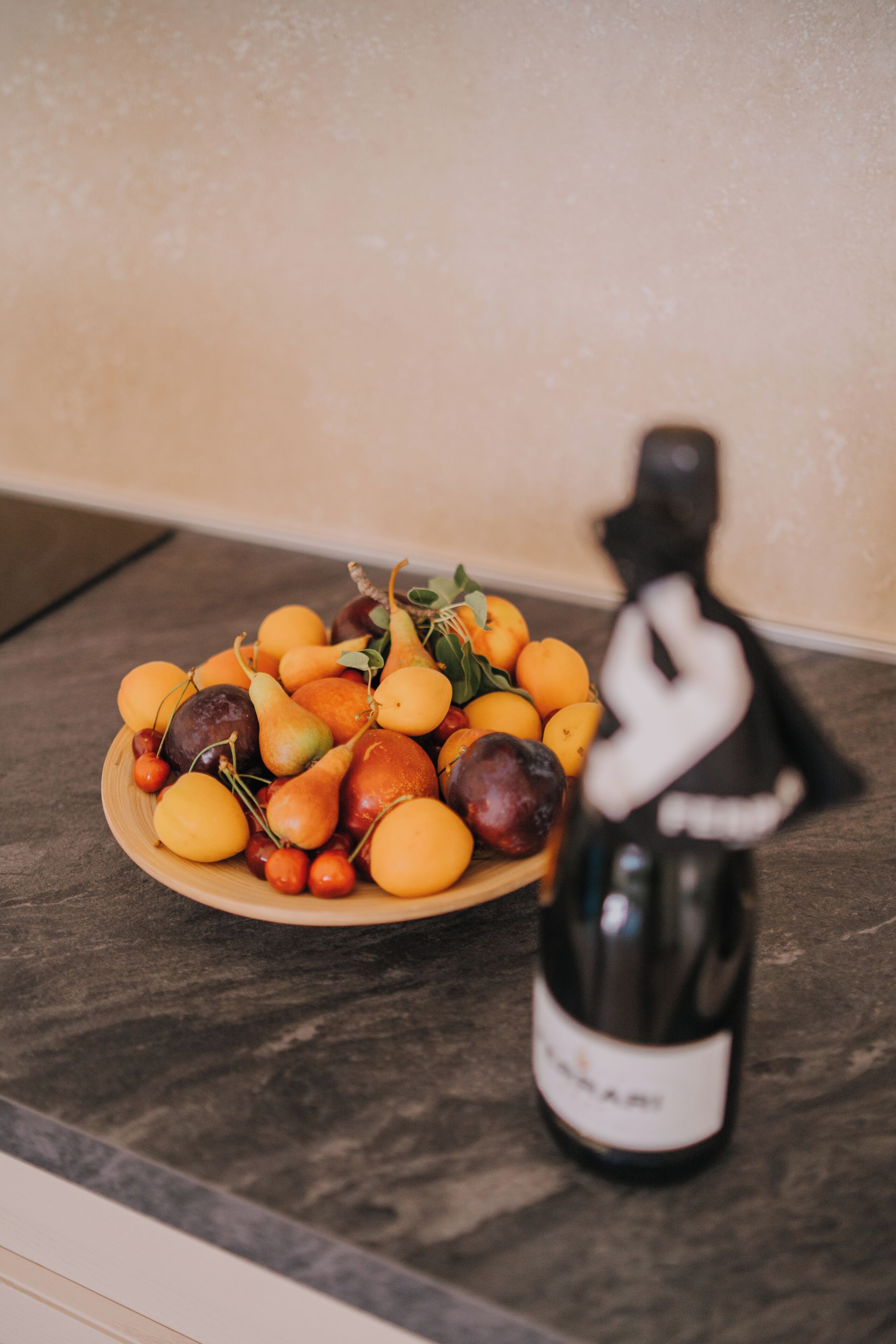 Een bord met fruit en een fles wijn op een donker aanrecht.