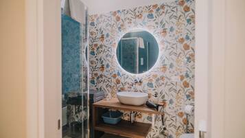 A bathroom with a round mirror, a wooden vanity, a blue basin, and floral wallpaper.