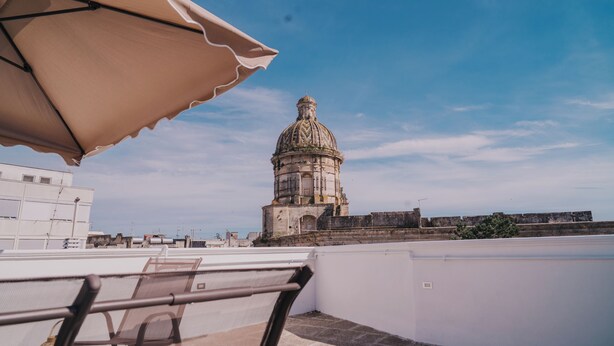 A rooftop terrace with a view of a historic building with a dome, a white railing, and a beige umbrella.