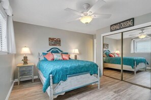 Une chambre à coucher comprenant un lit, deux tables de chevet, un ventilateur de plafond, un miroir et un panneau décoratif mural.