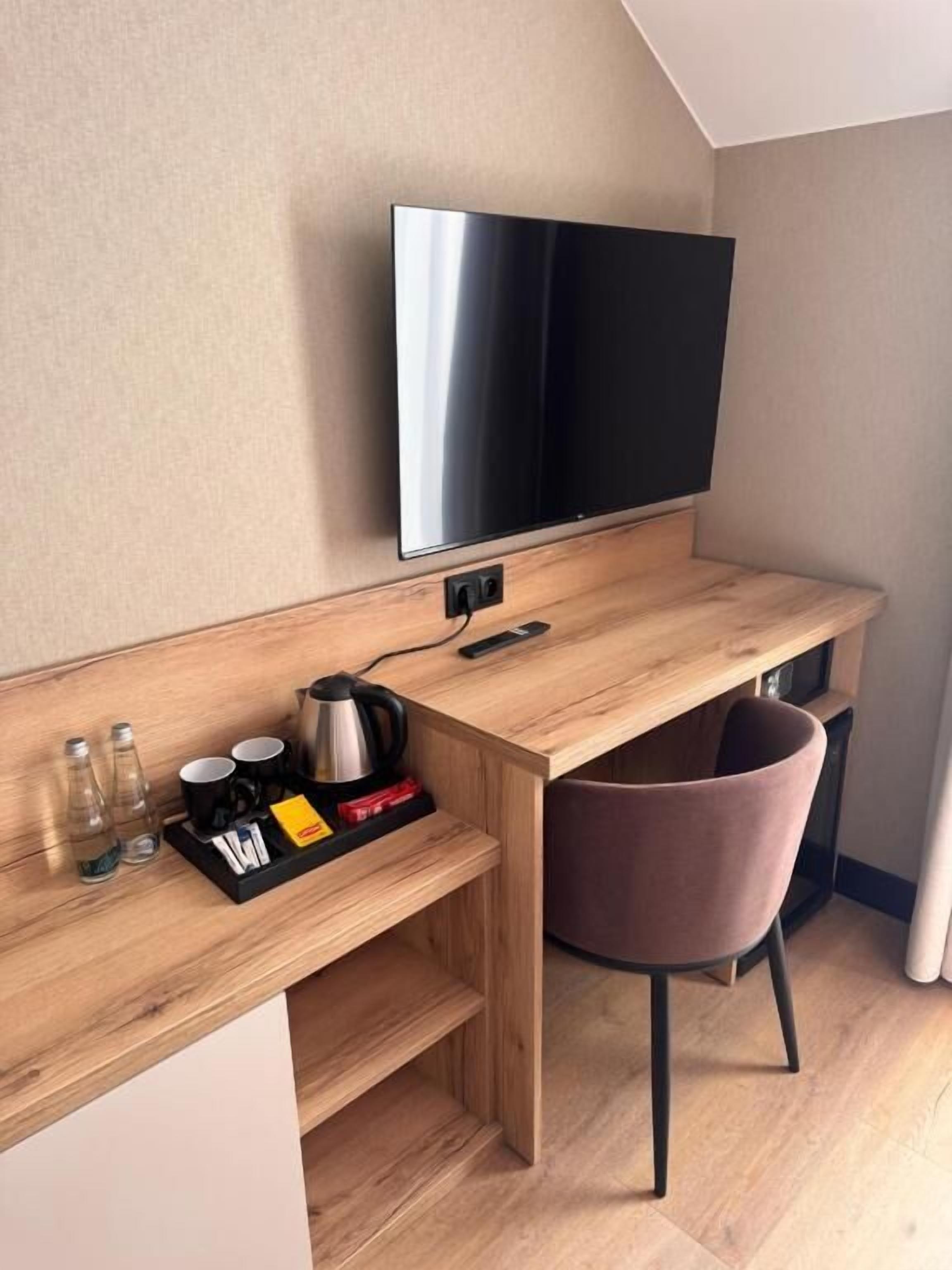 A modern hotel room with a wooden desk, a flat-screen TV, a chair, and a coffee maker.
