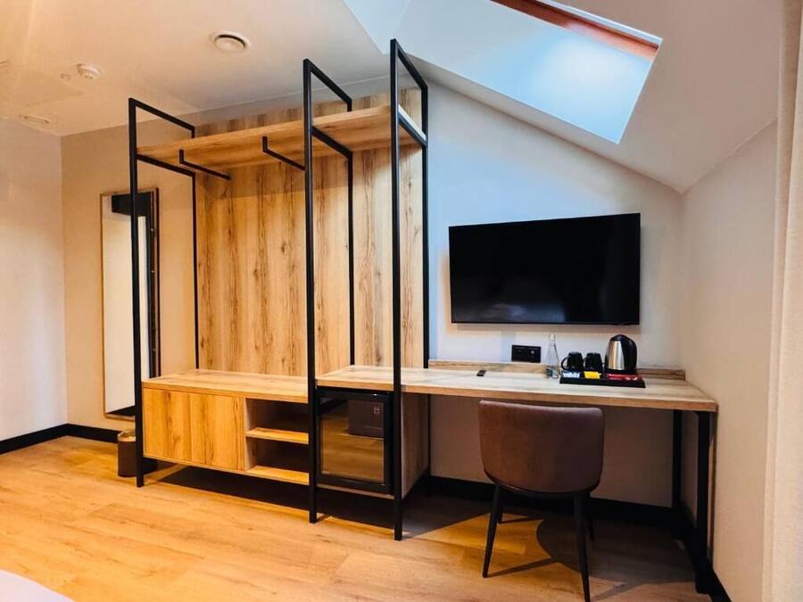 Una habitación moderna con un escritorio de madera, una silla, un televisor de pantalla plana y un tragaluz.