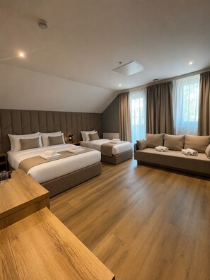 Quarto de hotel moderno com uma cama grande, um sofá, uma mesa de madeira e vista para o exterior pelas janelas.