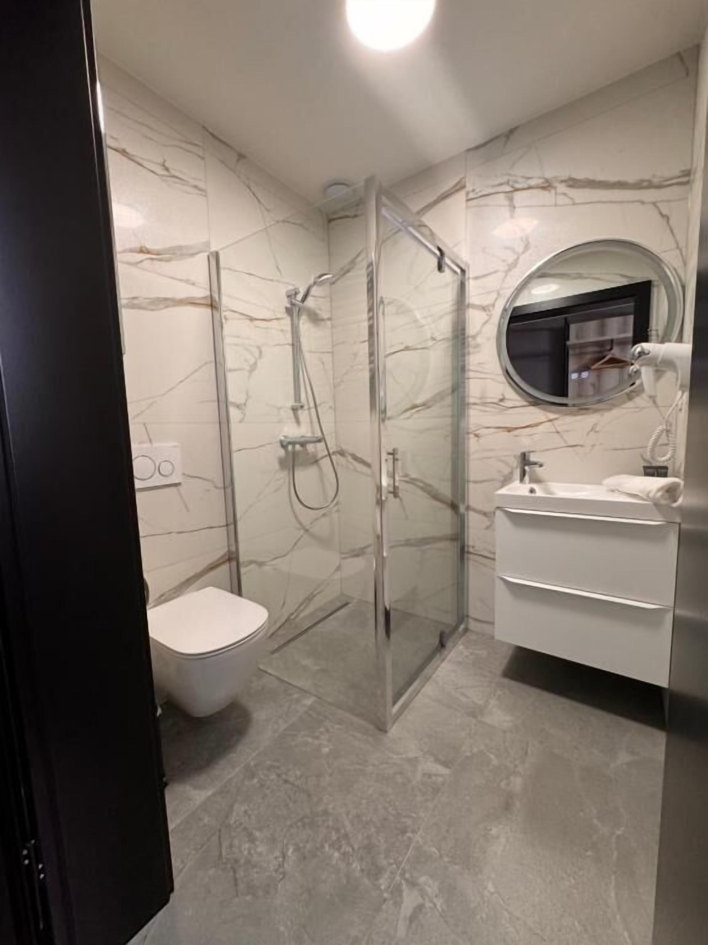 A bathroom with a glass-enclosed shower, a toilet, a sink, and a mirror.