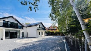Moderni rakennus, jossa on asfaltoitu ajotie, autotalli ja puilla reunustettu kävelyreitti.