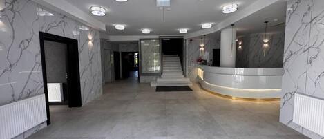 A modern lobby with marble walls, a reception desk, and a staircase leading to upper floors.