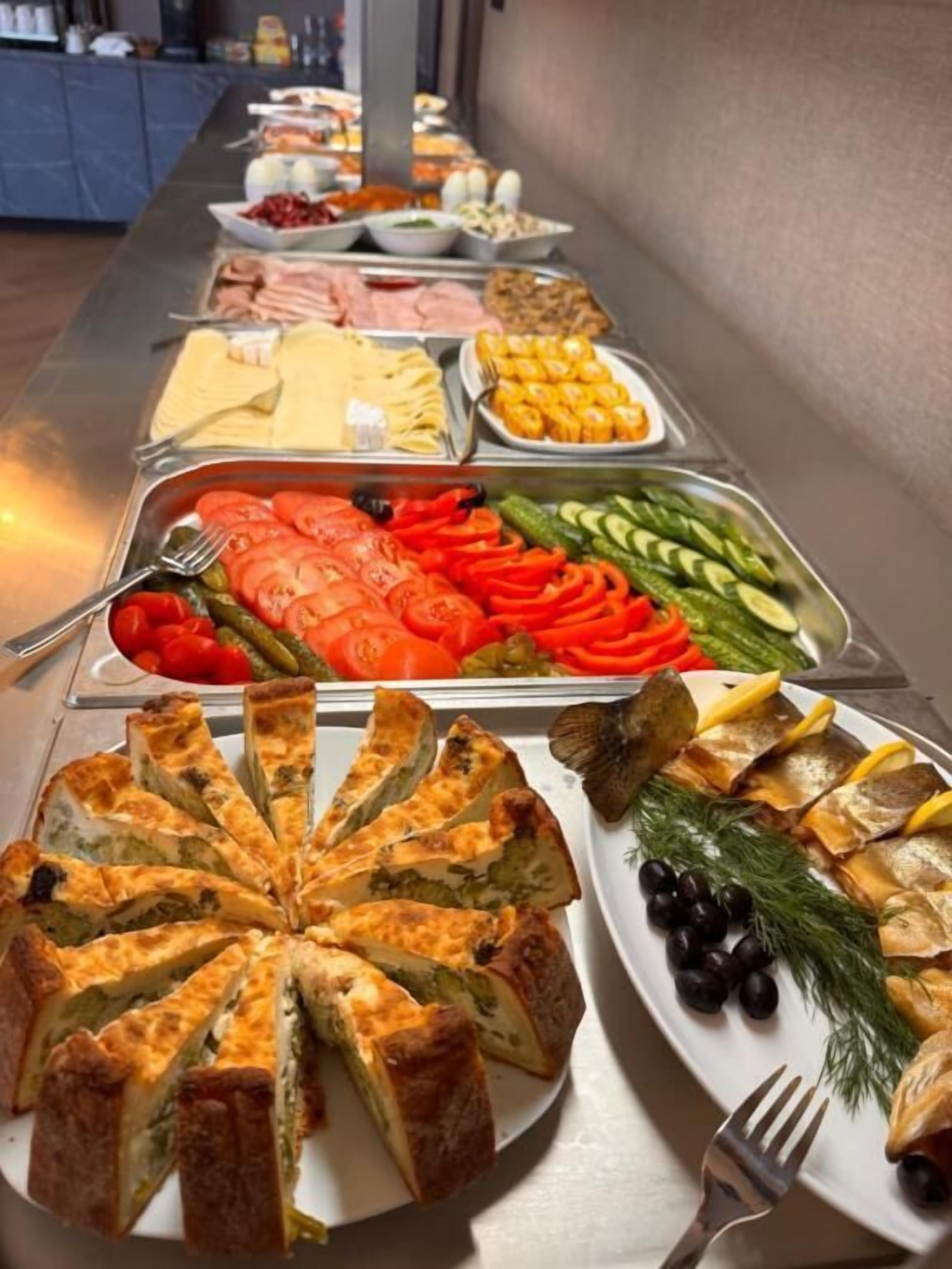 A buffet with various food options including sliced tomatoes, cucumbers, olives, and a fish dish.
