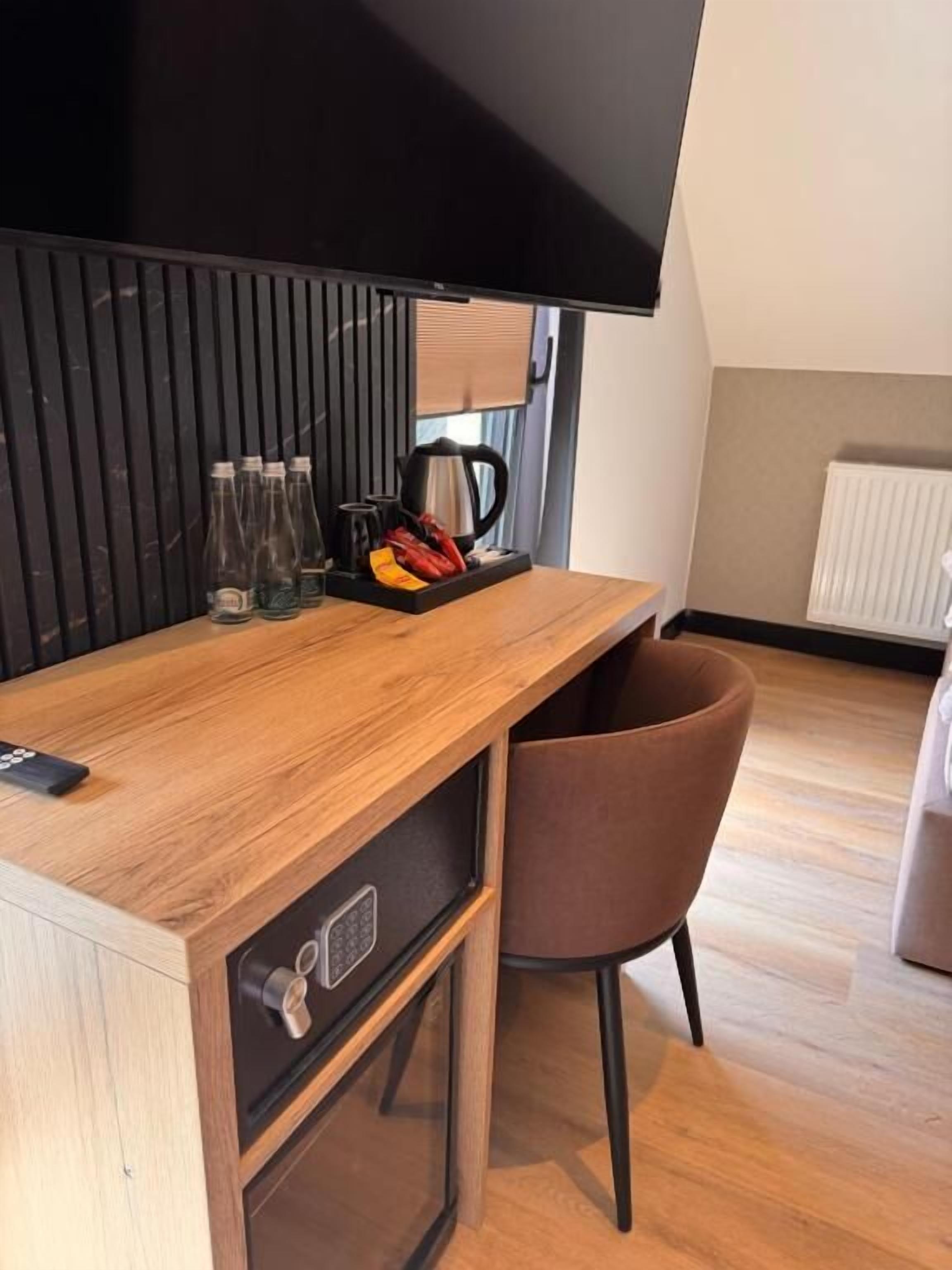 Un petit coin cuisine avec un plan de travail en bois, une machine à café et une bouilloire. On y trouve une chaise marron et un téléviseur fixé au mur.