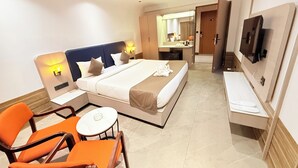 Quarto de hotel com cama, escrivaninha, cadeira, televisão e ventoinha no teto.