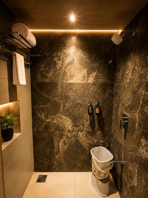 A modern bathroom with a marble wall, a toilet, a shower, and a towel rack.