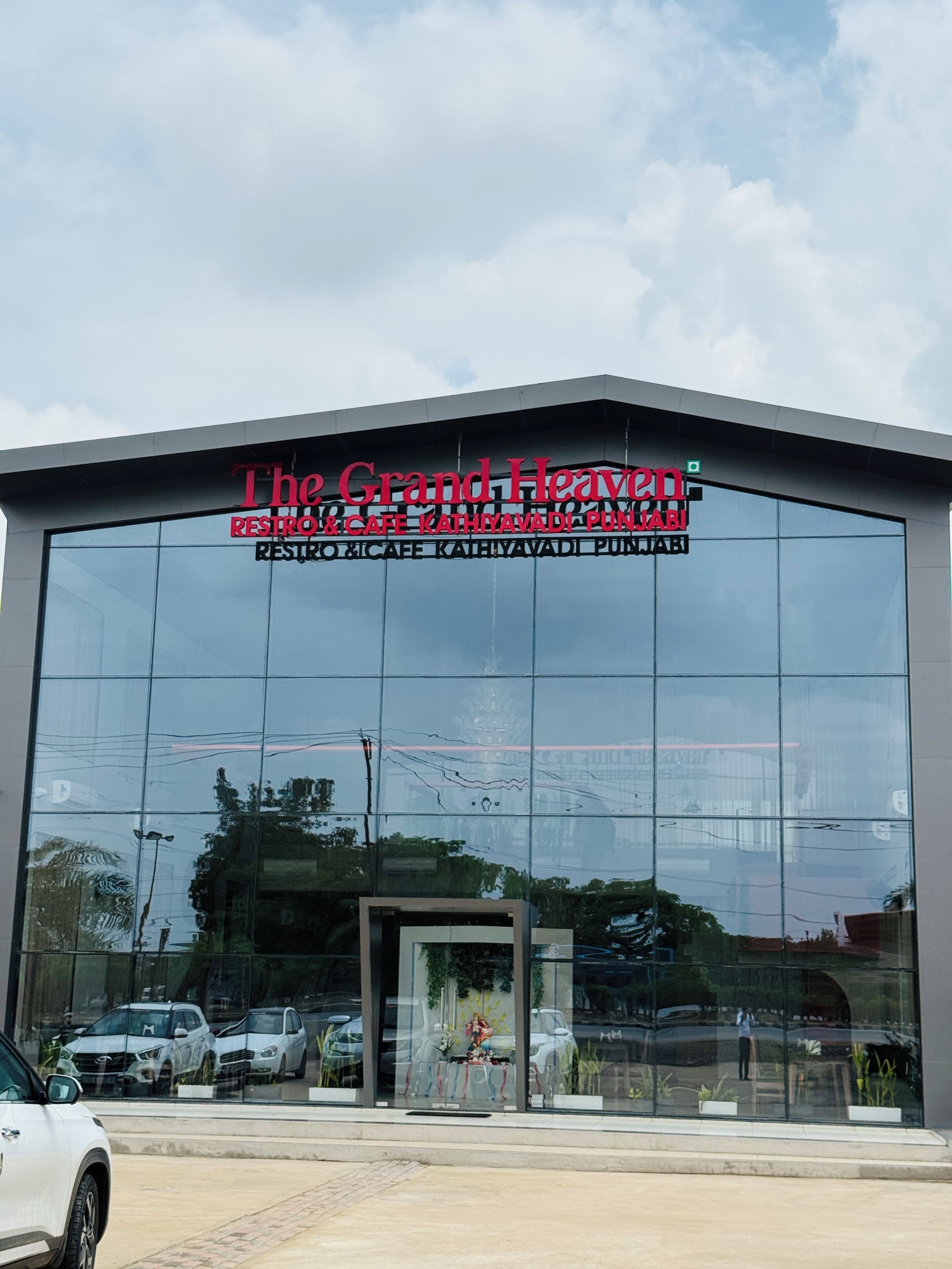 Um edifício moderno com fachada de vidro extensa e uma placa que diz 'The Grand Haven Restroom & Cafe Kathiyavadi Punnabi'.